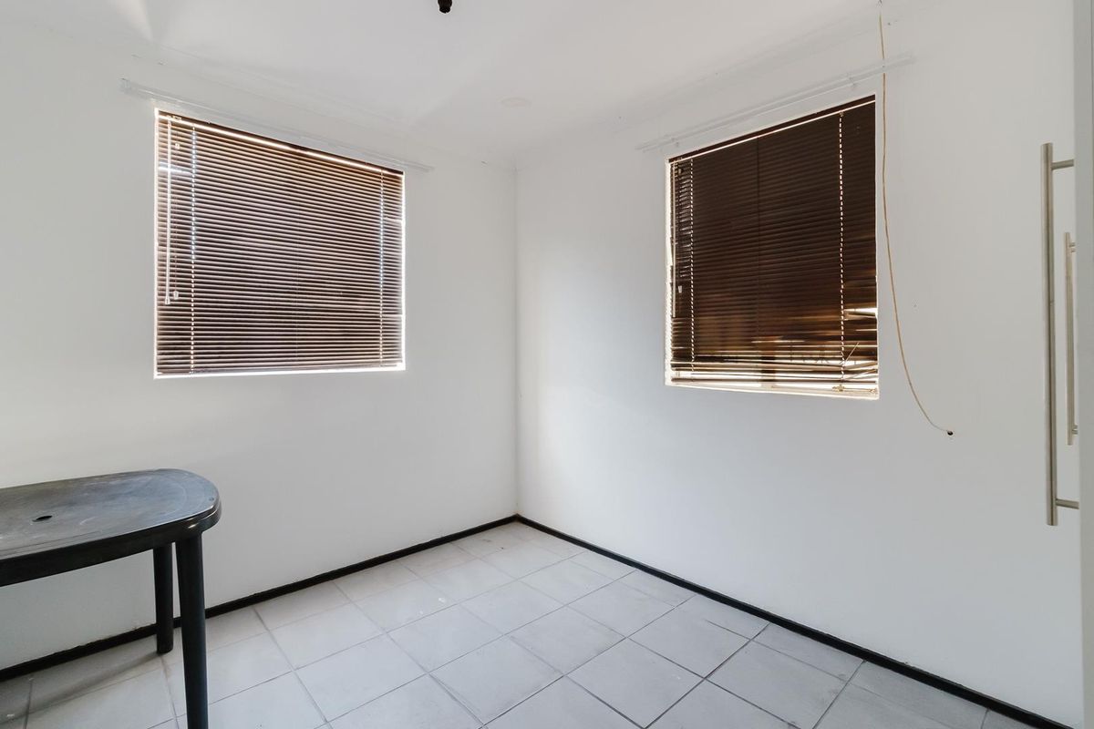A simple, empty bedroom featuring neutral tiled flooring and two windows fitted with venetian blinds.
