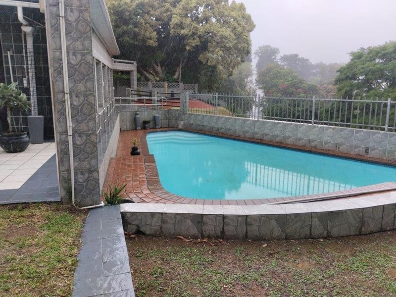 Outdoor pool area featuring a tiled surround, metal perimeter fencing, and stone-clad exterior wall, set within a landscaped garden environment.