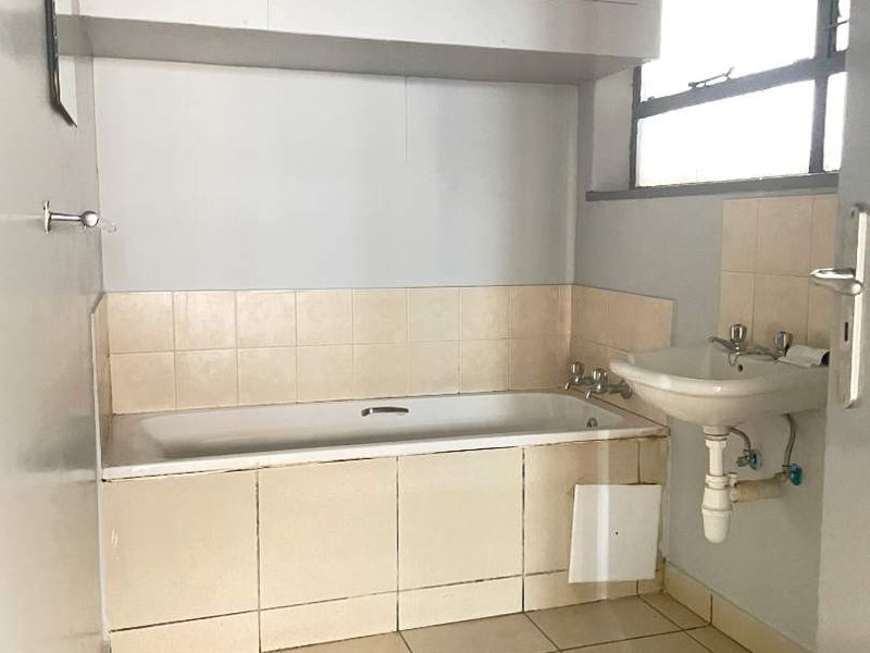 A functional bathroom featuring a bathtub, wall-mounted basin, and built-in overhead storage, requiring cosmetic updates to improve its overall condition and aesthetic appeal.