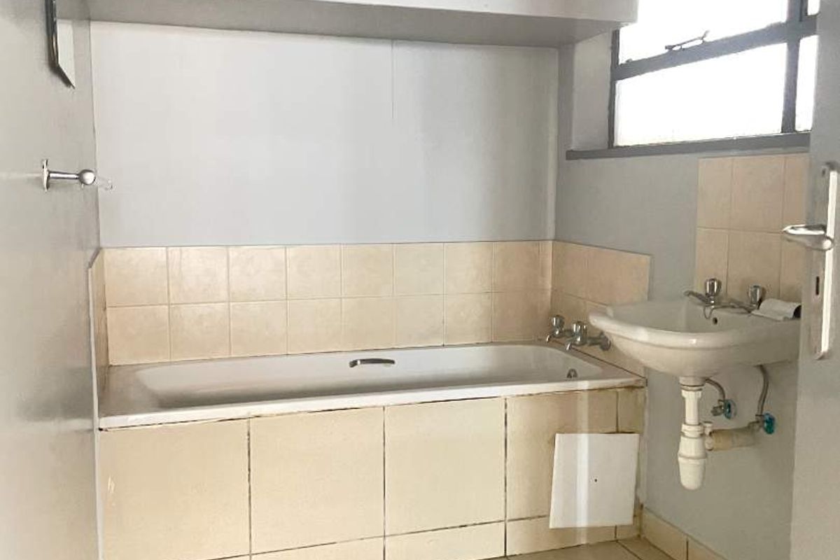 A functional bathroom featuring a bathtub, wall-mounted basin, and built-in overhead storage, requiring cosmetic updates to improve its overall condition and aesthetic appeal.