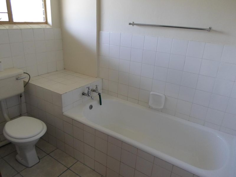 A functional bathroom featuring a built-in bathtub, toilet, and tiled splashbacks, offering a blank canvas for potential modernization and renovation.