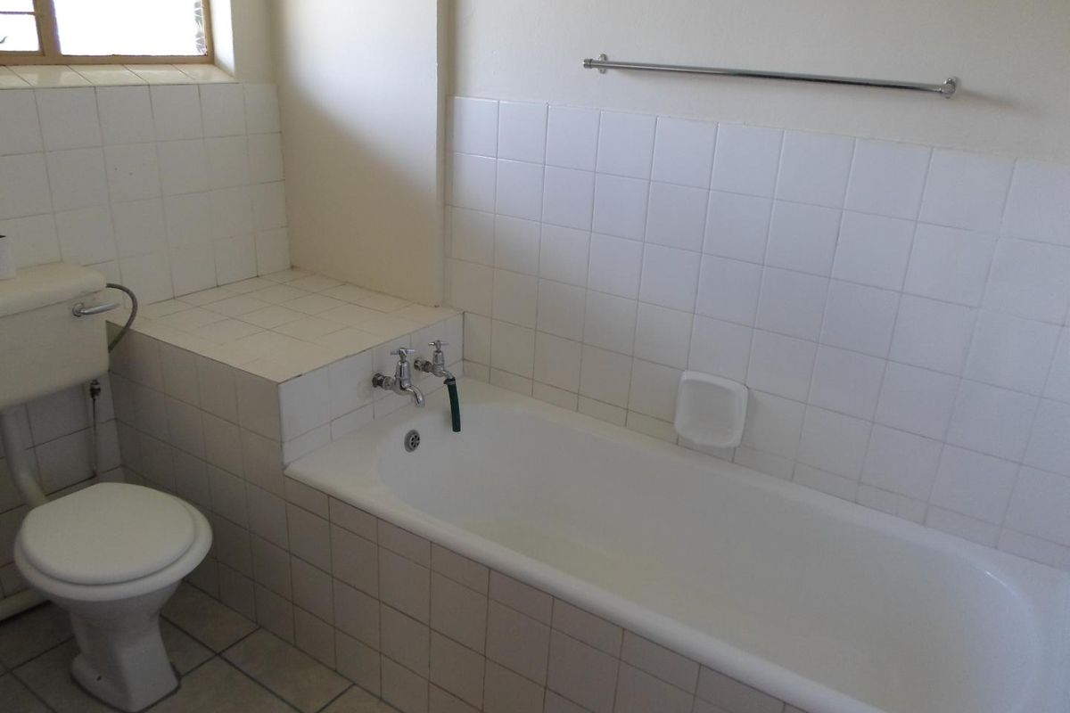 A functional bathroom featuring a built-in bathtub, toilet, and tiled splashbacks, offering a blank canvas for potential modernization and renovation.