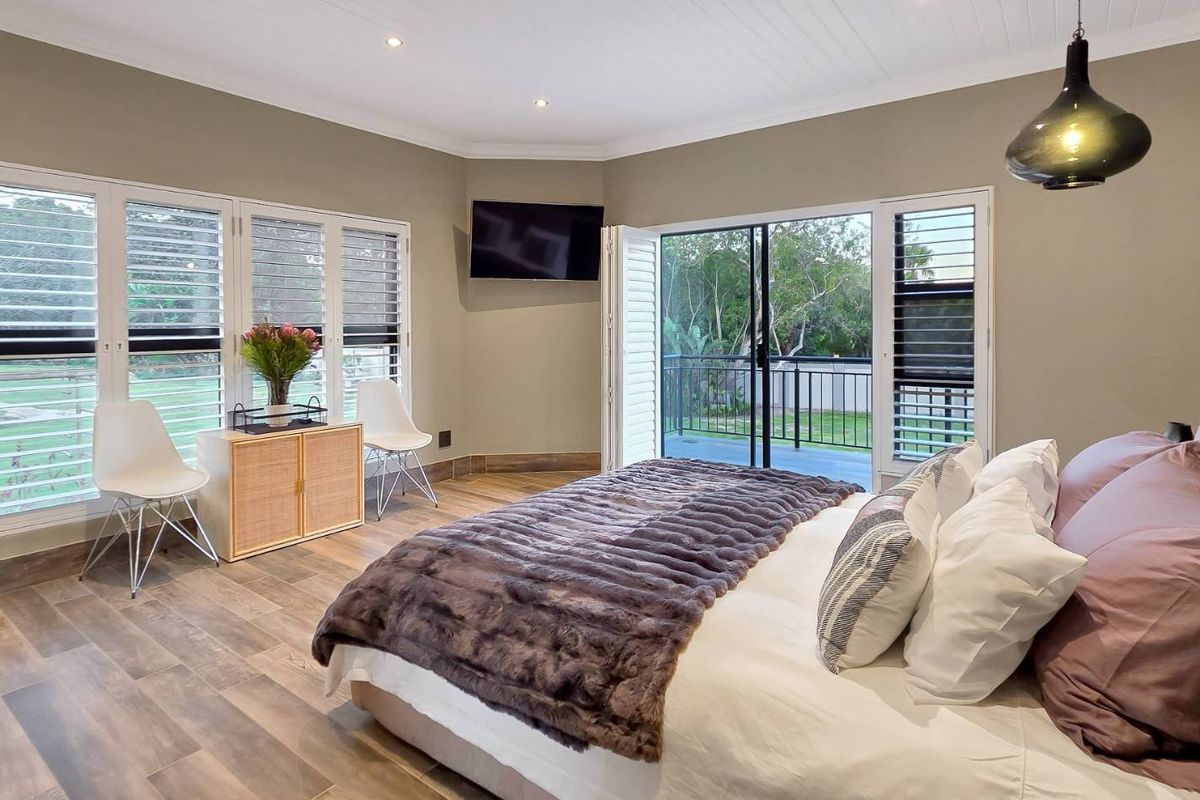Spacious bedroom featuring wood-look tile flooring, plantation shutters, recessed lighting, and direct access to a private balcony through sliding glass doors.