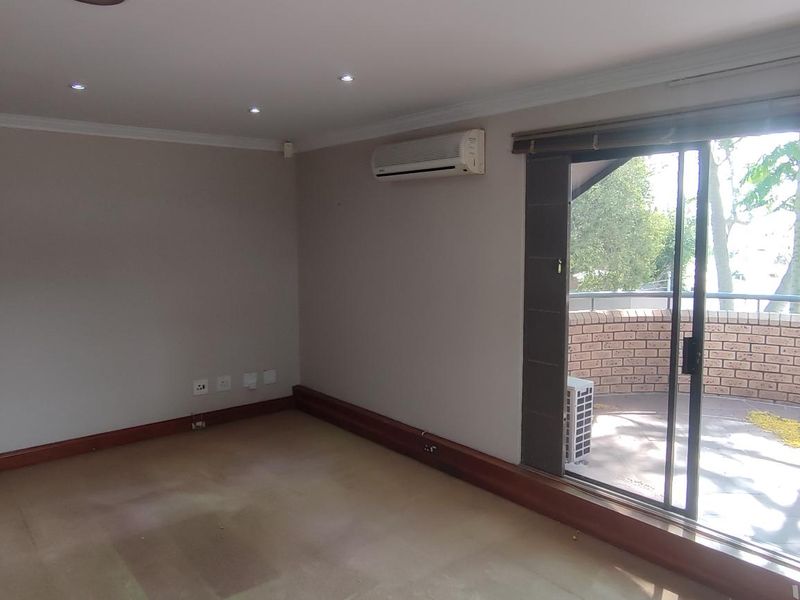 An empty office space featuring recessed lighting, a wall-mounted air conditioning unit, and a sliding glass door leading to an outdoor balcony area.