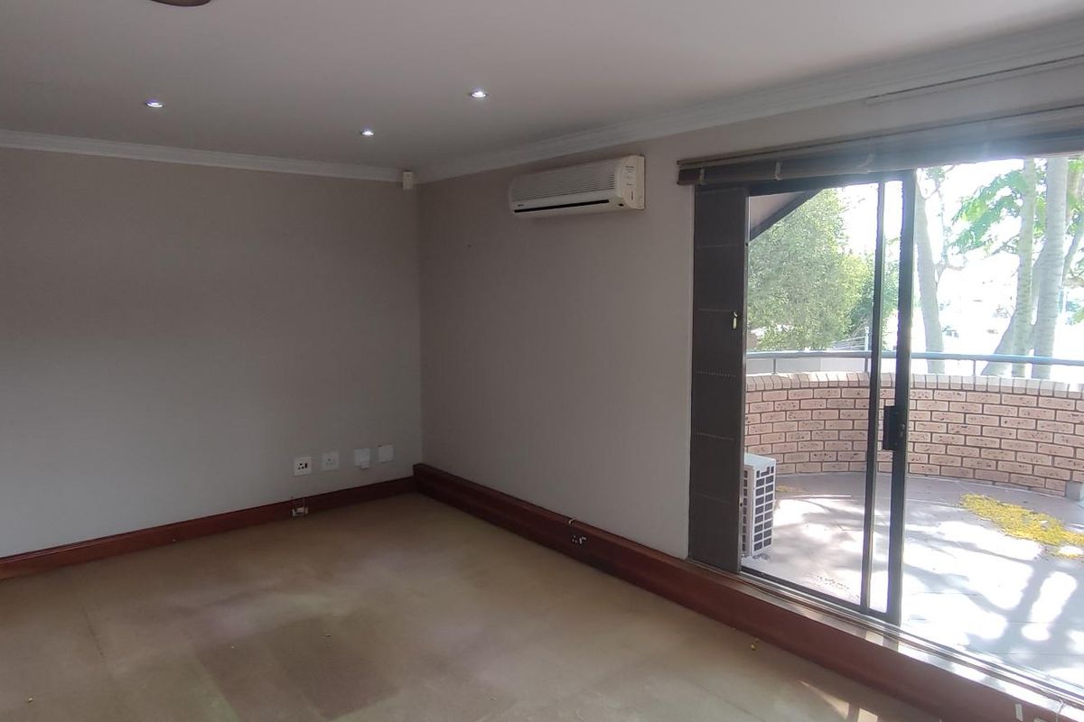 An empty office space featuring recessed lighting, a wall-mounted air conditioning unit, and a sliding glass door leading to an outdoor balcony area.