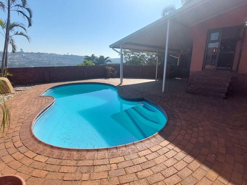 Outdoor pool area featuring a kidney-shaped swimming pool, brick paving, and a covered patio space with scenic views.