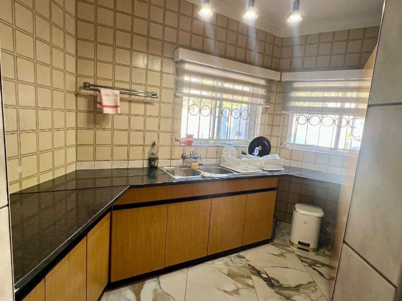 A functional kitchen featuring granite countertops, wood-finish cabinetry, marble-look floor tiles, and a double basin sink with modern pendant lighting.