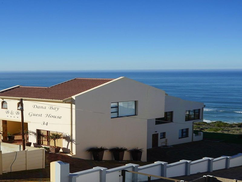 Front elevation of a multi-level guest house featuring a tiled roof and boundary wall, situated with prominent ocean views.