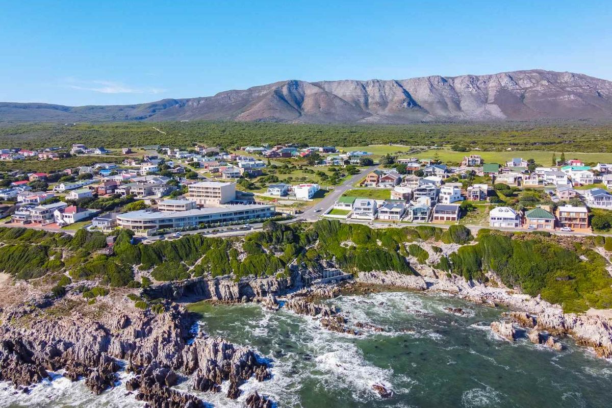 An aerial view of a coastal residential neighborhood situated along a rocky shoreline with a mountain range in the background.