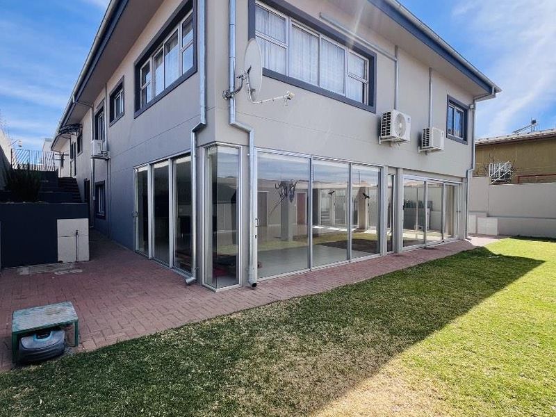 Rear view of a two-story house featuring extensive sliding glass doors, paved patio area, and a well-maintained lawn.