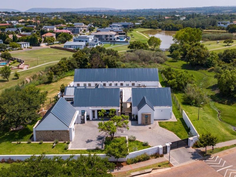 Aerial view of a modern residential property featuring a multi-wing metal roof design, paved driveway, and landscaped grounds within a secure estate.