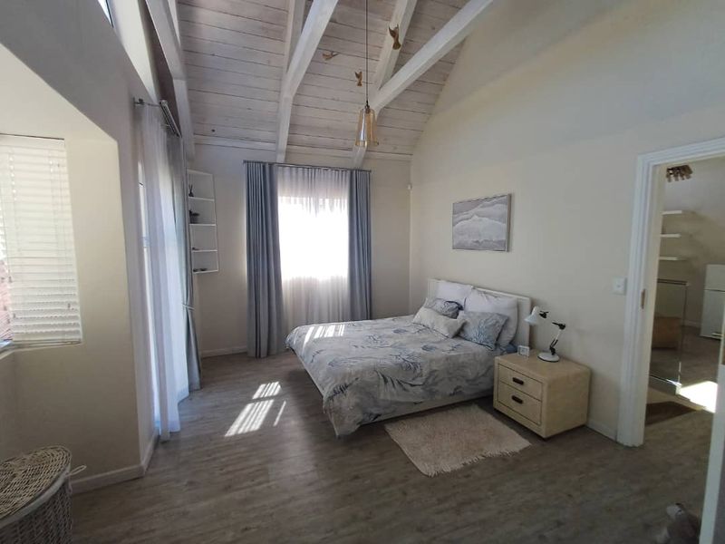 A bright bedroom featuring high vaulted ceilings with exposed timber beams, laminate flooring, and large windows allowing for ample natural light.