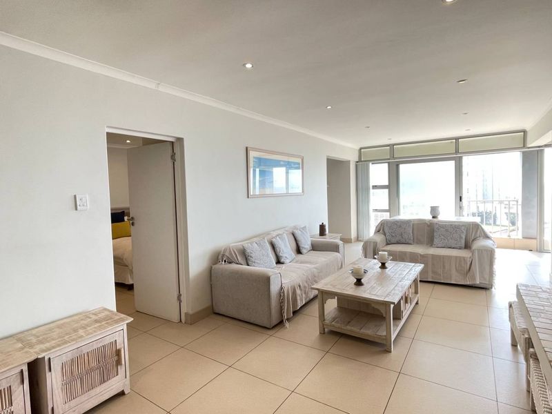 Spacious open-plan living area featuring neutral tiled flooring, recessed lighting, and large sliding glass doors providing access to the balcony.
