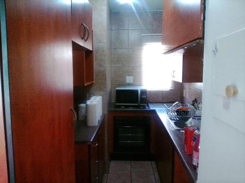 A compact galley-style kitchen featuring built-in wooden cabinetry, a built-in oven, hob, and tiled finishes, offering a functional layout for efficient meal preparation.