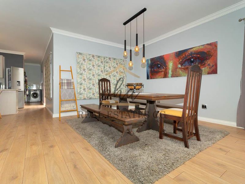 Open plan dining area featuring laminate flooring, crown molding, and modern pendant lighting, seamlessly connected to a functional kitchen space.