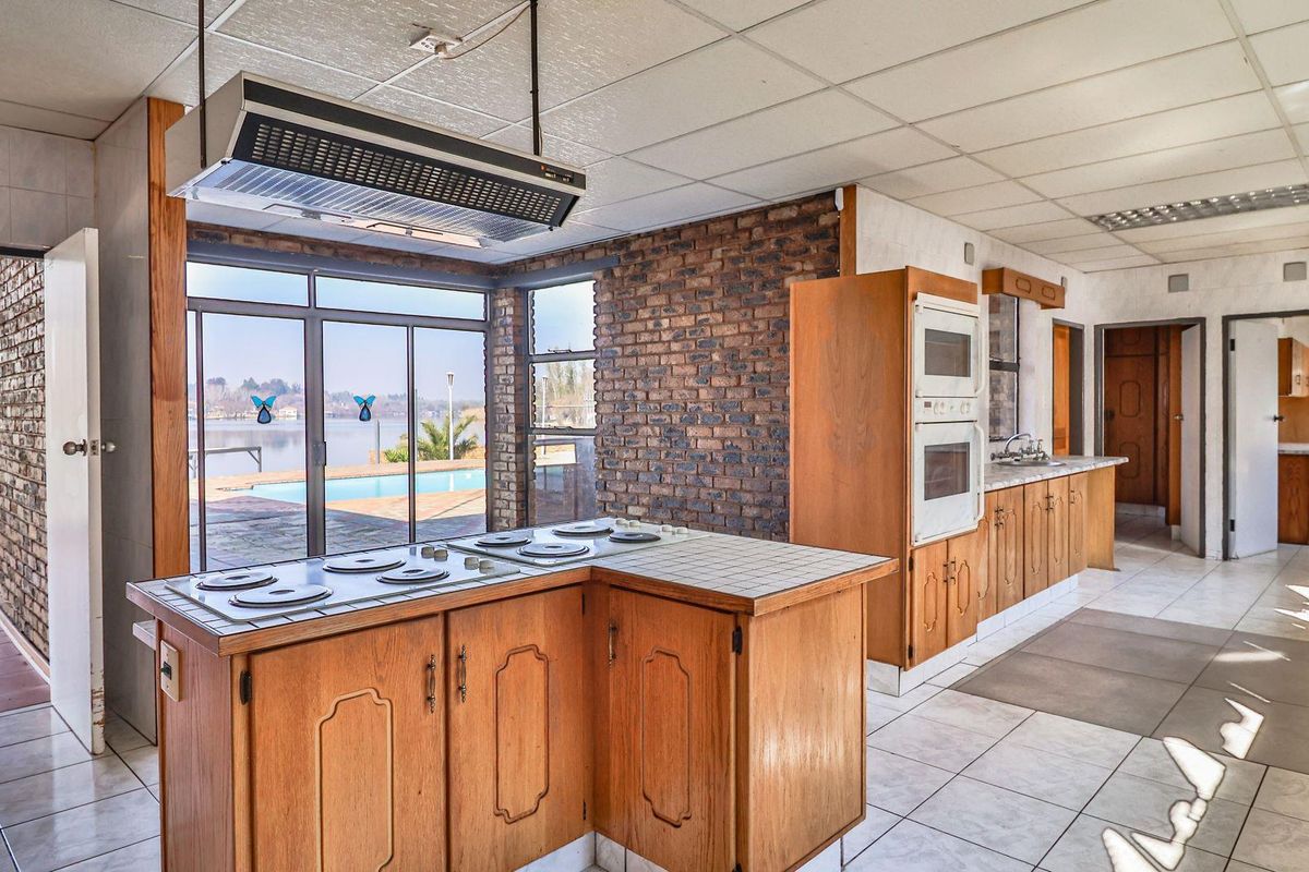 Spacious kitchen featuring wooden cabinetry, built-in double oven, electric hob, and exposed brick walls, with direct access to the outdoor pool area.