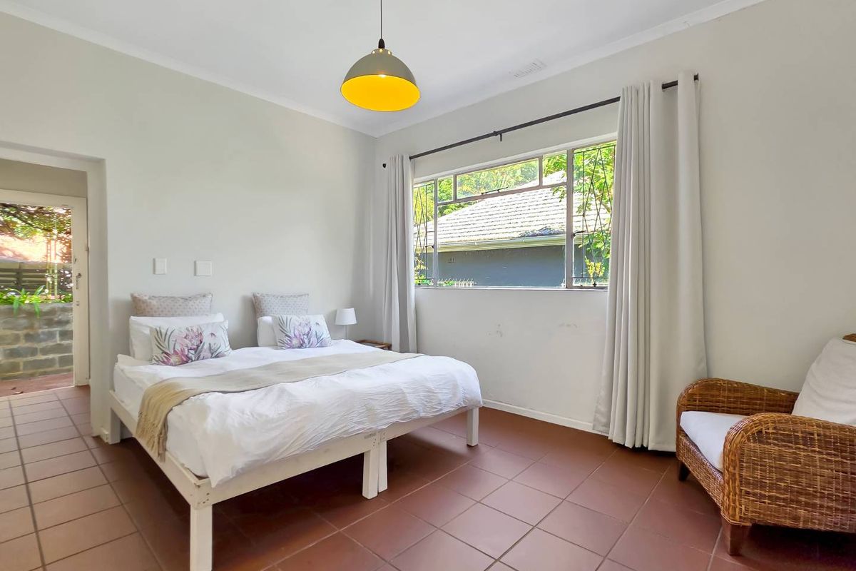 A bright bedroom featuring tiled flooring, a large window with security bars, and a pendant light fixture.