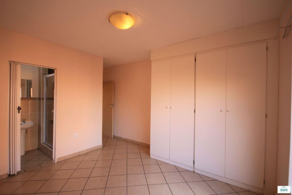 A spacious bedroom featuring neutral tiled flooring, ample built-in cupboard storage, and direct access to an en-suite bathroom.
