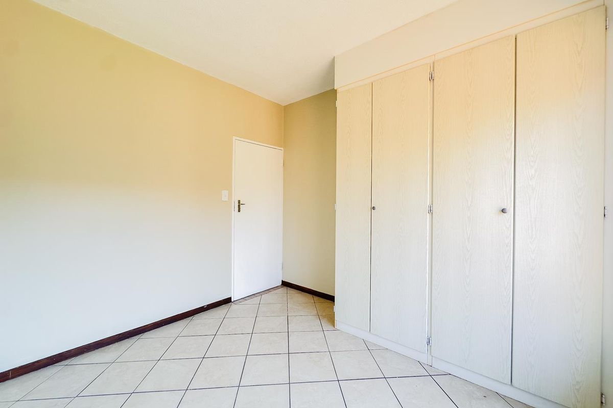 A bright, empty bedroom featuring neutral walls, tiled flooring, and built-in wooden cabinetry providing ample storage space.