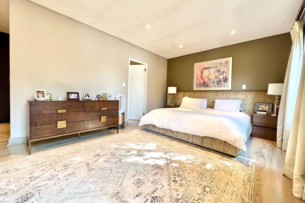 A spacious bedroom featuring light wood-look flooring, recessed ceiling lighting, and a neutral color palette with an accent wall.