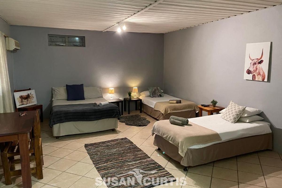 Spacious guest bedroom featuring tiled flooring, neutral wall tones, and a corrugated ceiling finish, providing a functional layout for multiple guests.