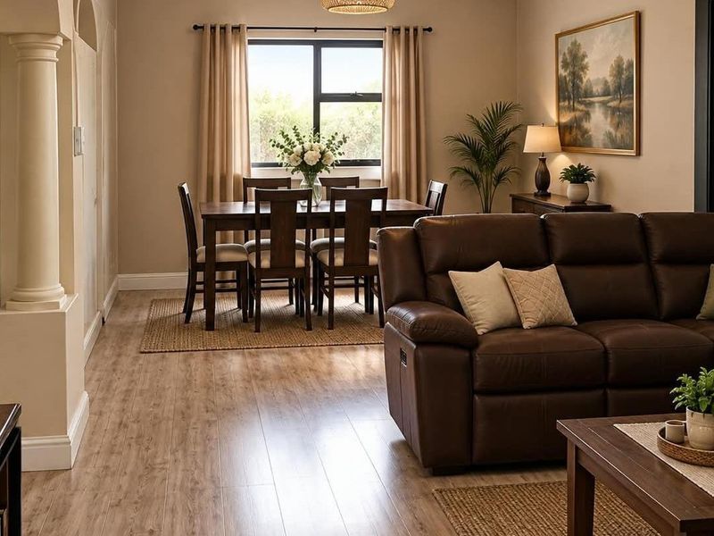 An inviting open-plan living and dining area featuring warm laminate flooring, a decorative architectural column, and natural light through a central window.