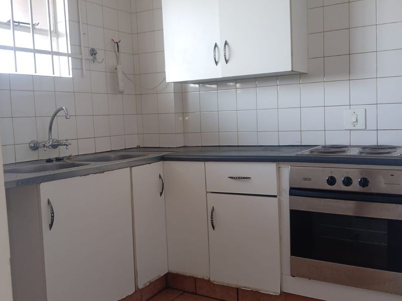 A functional kitchen featuring built-in cabinetry, a stainless steel sink, and an integrated oven with hob, finished with a tiled backsplash.