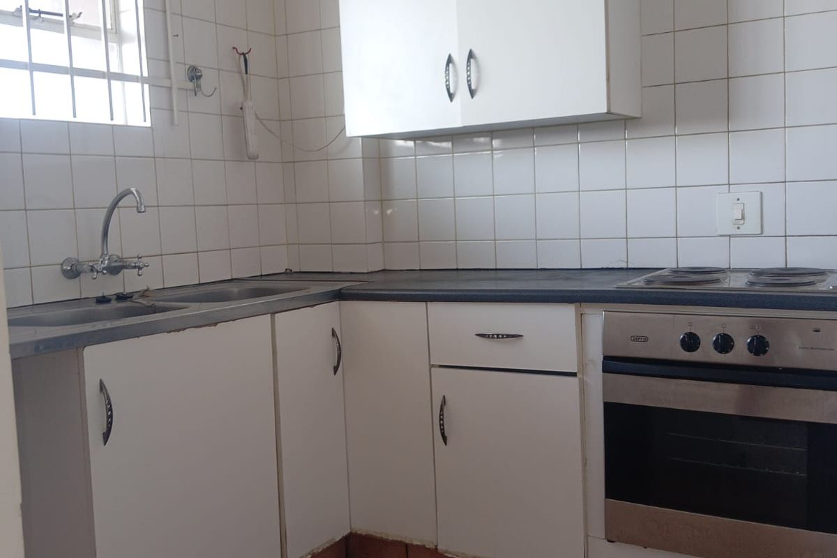 A functional kitchen featuring built-in cabinetry, a stainless steel sink, and an integrated oven with hob, finished with a tiled backsplash.