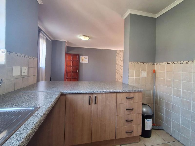 A functional kitchen area featuring laminate cabinetry, granite-look countertops, and neutral ceramic wall and floor tiling, offering a clean and practical workspace.