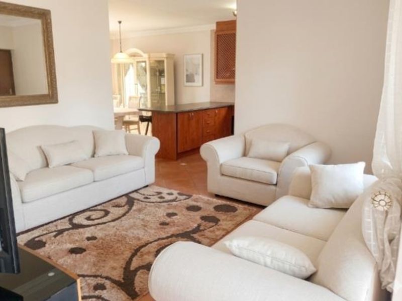 Open-plan living area featuring tiled flooring and a connected kitchen space with wooden cabinetry and a central island.