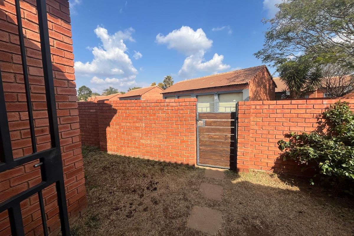 A private rear courtyard area featuring a brick boundary wall, a timber pedestrian gate, and paved stepping stones leading through the garden space.