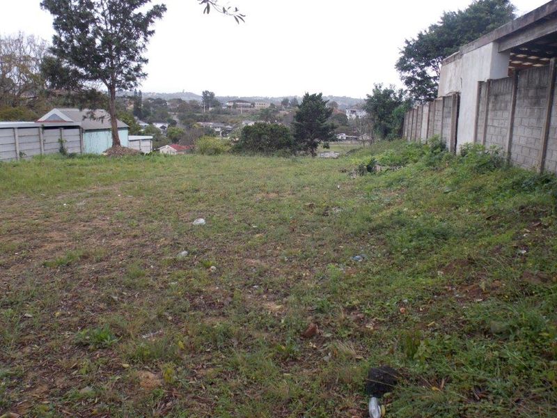A view of a vacant residential plot featuring a boundary wall and surrounding neighborhood landscape.