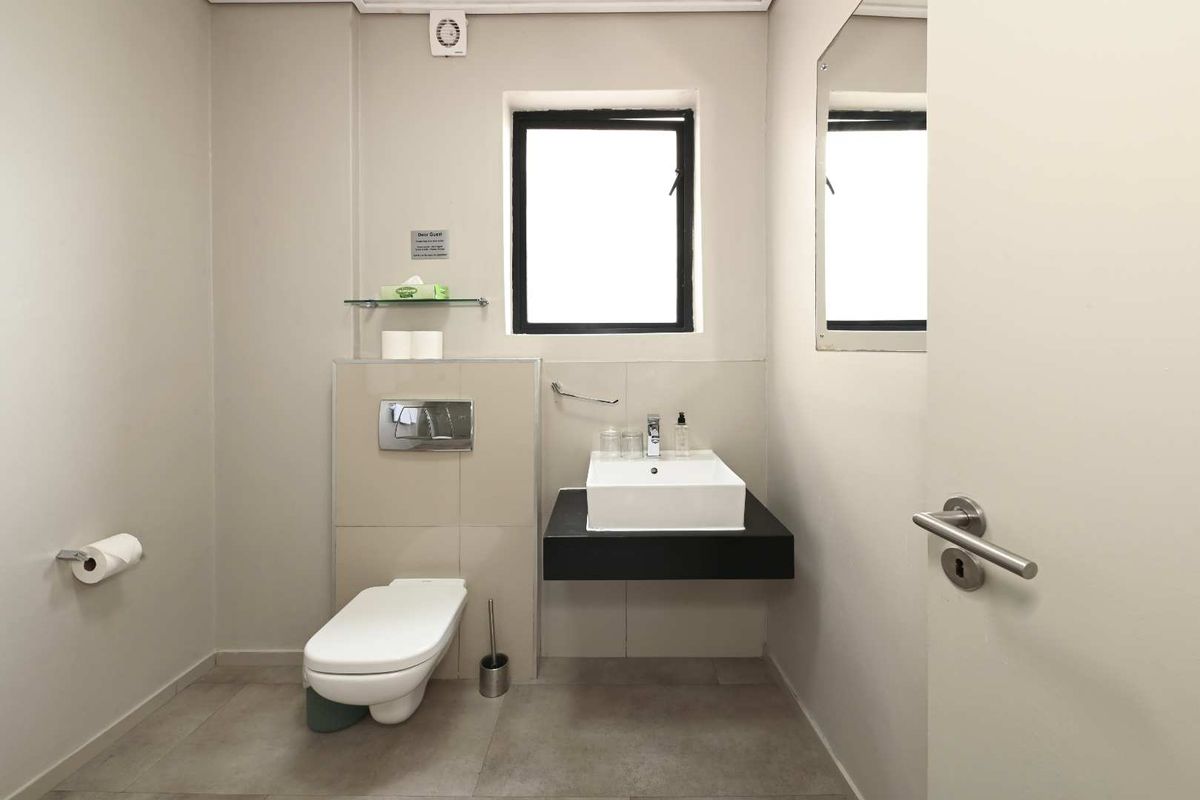A modern guest bathroom featuring a wall-mounted toilet, a floating vanity with a square basin, and neutral floor tiling.