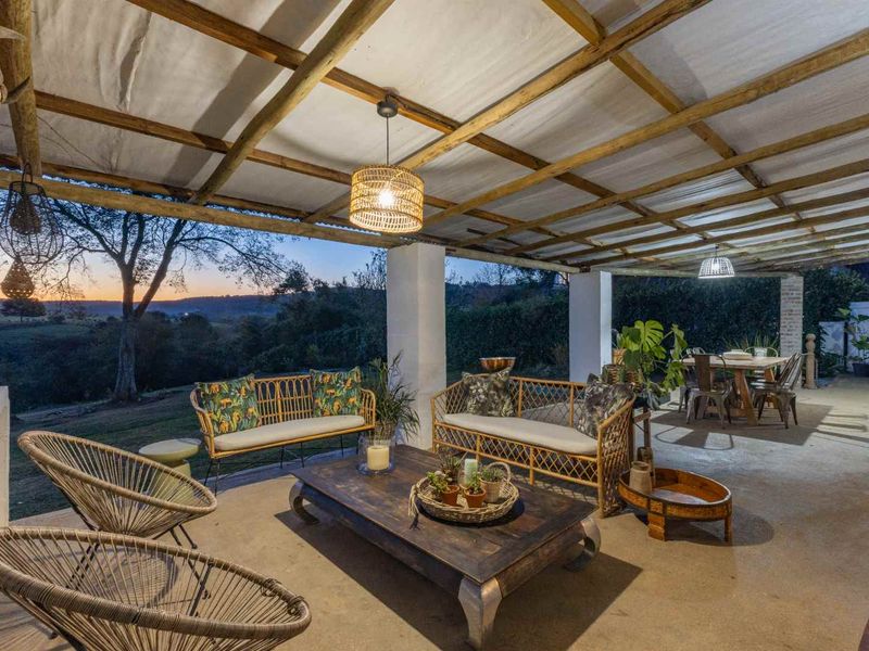 Spacious covered patio featuring a timber pergola, concrete flooring, and a brick fireplace, offering scenic views of the surrounding landscape.