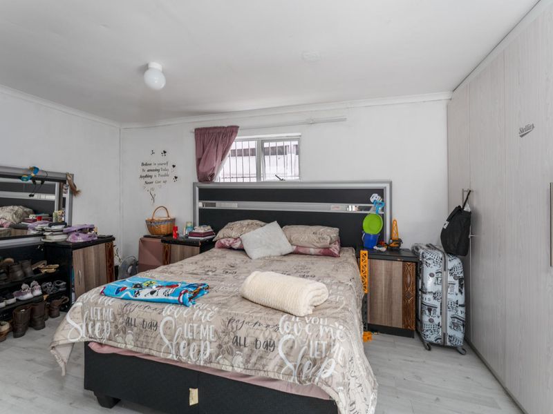 A functional bedroom featuring built-in cupboards and a window with security bars, offering a practical layout for a comfortable living space.