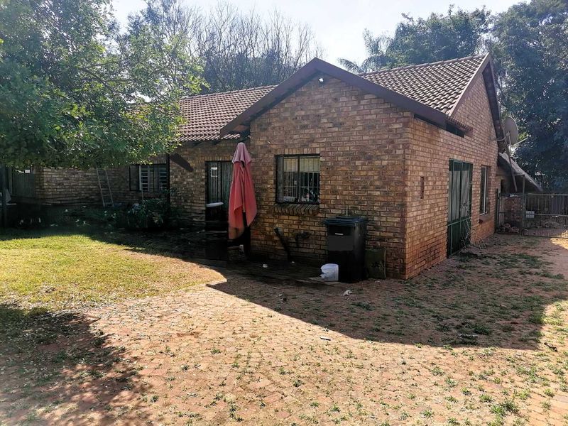 Rear view of a face brick house featuring a tiled roof, security bars on windows, and a paved outdoor patio area.