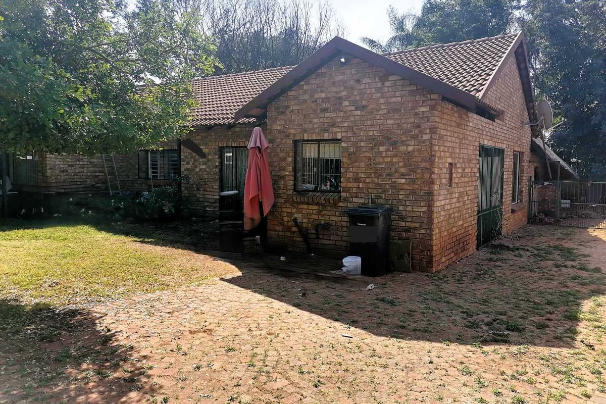 Rear view of a face brick house featuring a tiled roof, security bars on windows, and a paved outdoor patio area.