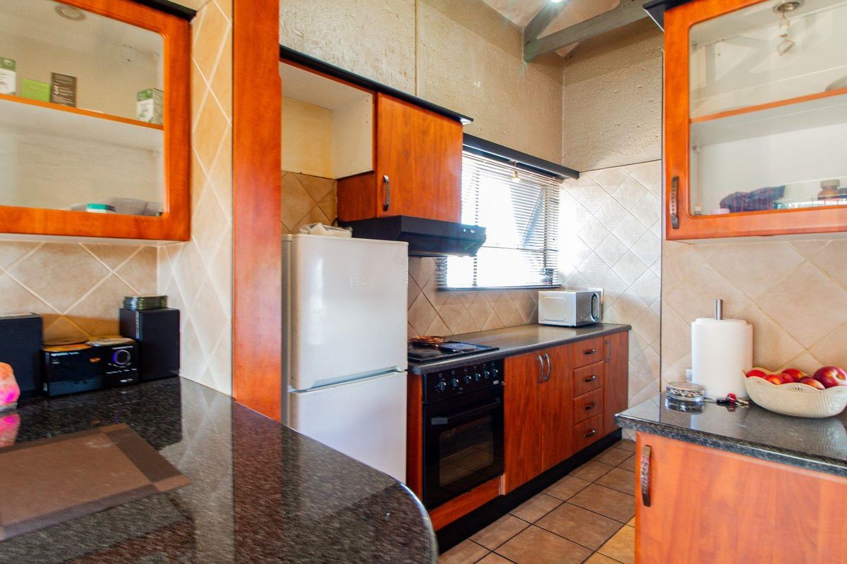 A functional kitchen featuring wood-finish cabinetry, granite countertops, a built-in oven with extractor fan, and tiled flooring.