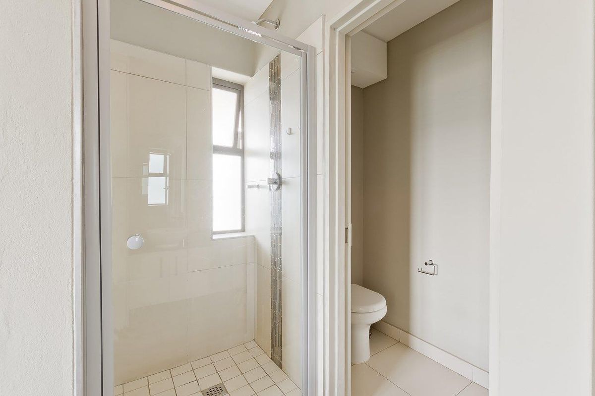 A clean bathroom featuring a glass-enclosed shower with tiled walls and a separate toilet area with neutral finishes.