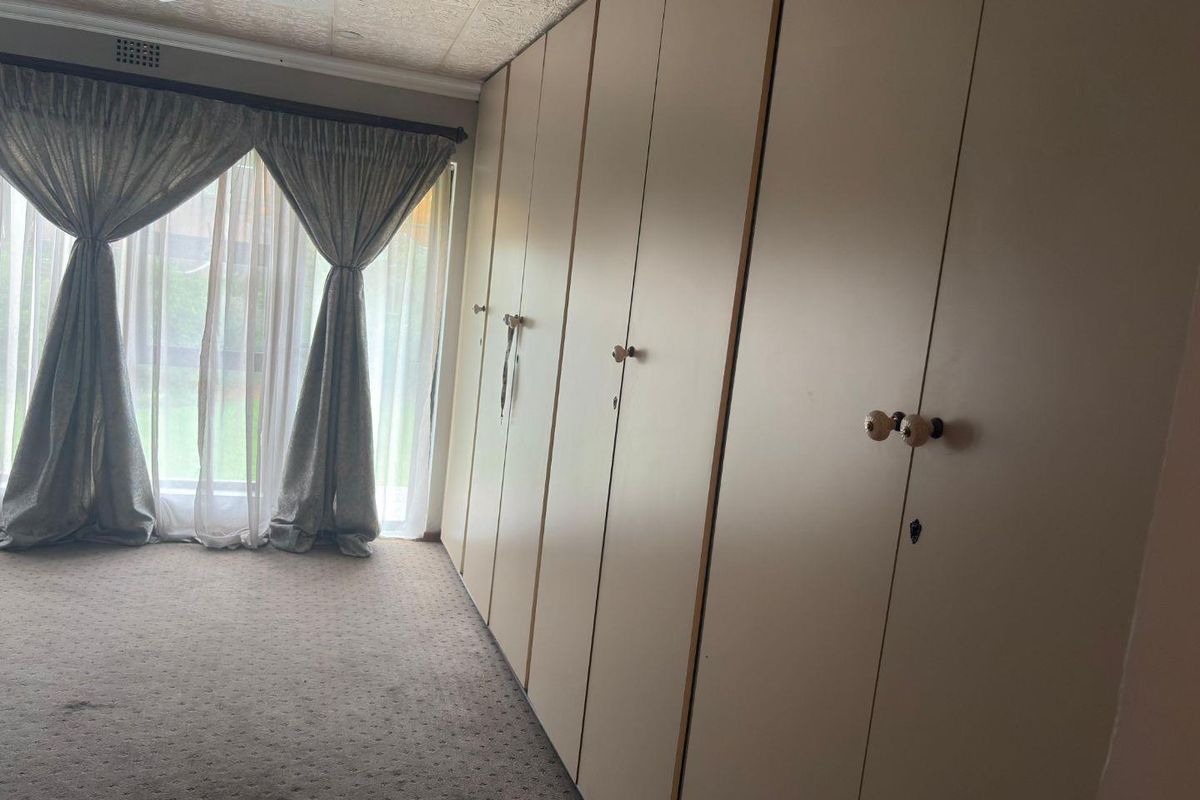 A bedroom featuring extensive wall-to-wall built-in cabinetry and large windows with curtains, providing ample storage space and natural light.