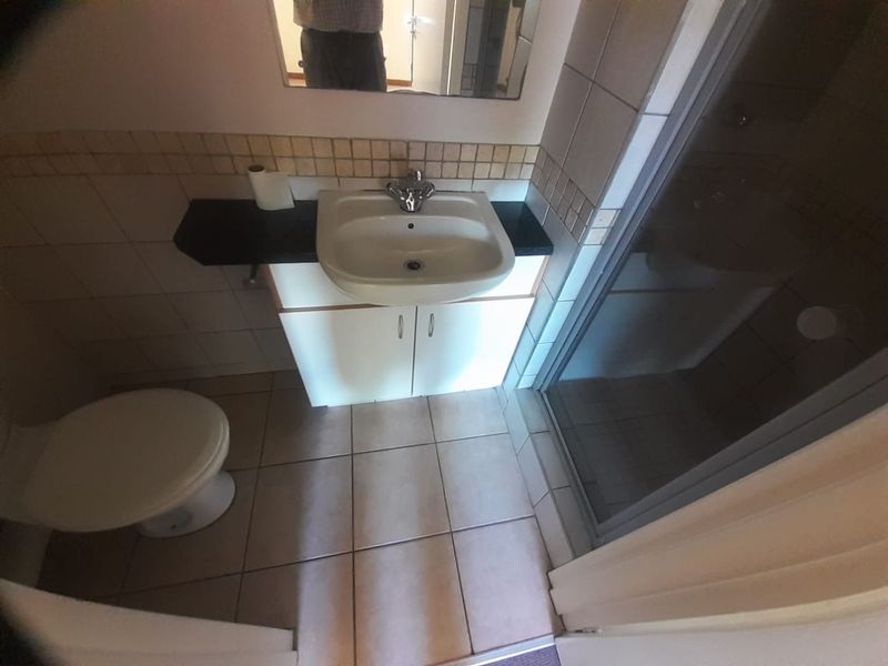 A functional bathroom featuring a vanity cabinet with a basin, a shower enclosure, and tiled flooring and walls.