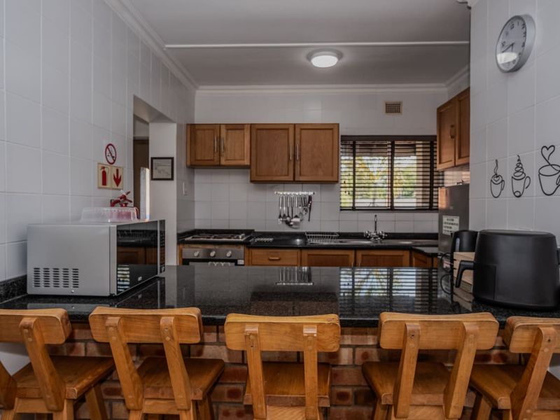 A functional kitchen featuring wooden cabinetry, granite countertops, a built-in gas hob and oven, and a brick-based breakfast bar.