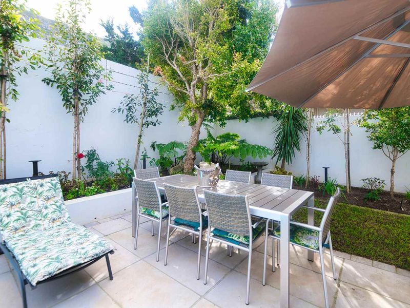 A well-maintained paved patio area featuring raised garden beds and a boundary wall, perfect for outdoor dining and relaxation.