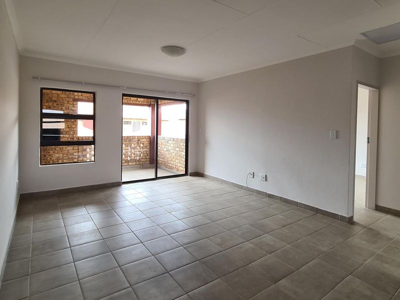 A bright, empty living room featuring neutral tiled flooring, large windows, and a sliding door providing access to an outdoor balcony area.