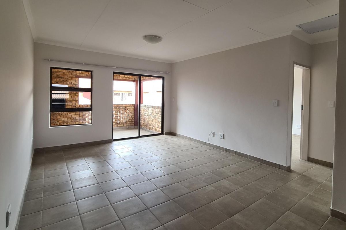 A bright, empty living room featuring neutral tiled flooring, large windows, and a sliding door providing access to an outdoor balcony area.