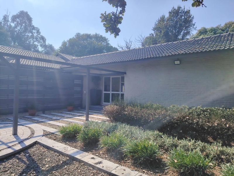 Front entrance view of the property featuring a painted brick facade, a modern pergola structure, and a neatly landscaped garden with paved pathways.