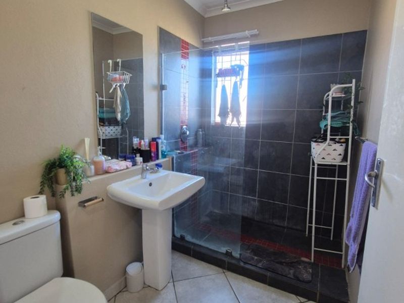 A functional bathroom featuring a pedestal basin, a walk-in shower with dark tiling, and ceramic floor tiles.