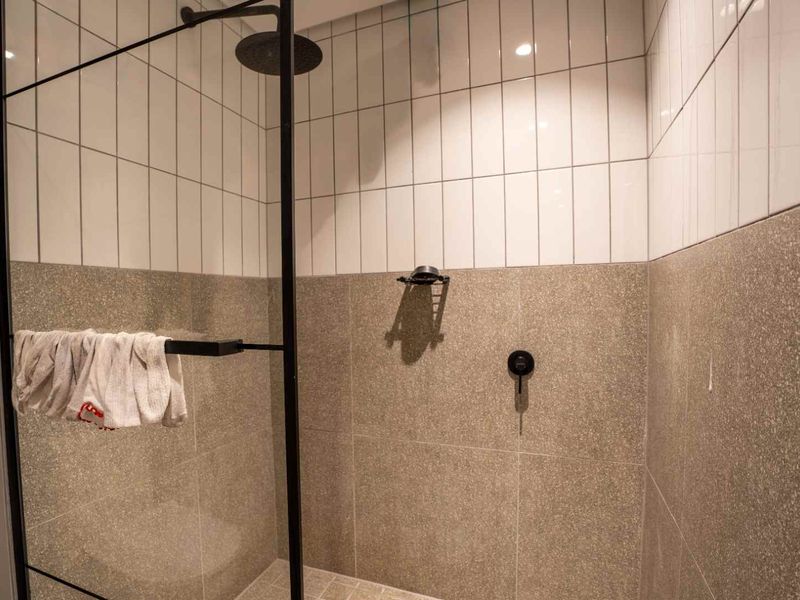 Modern walk-in shower featuring a black-framed glass screen, rain shower head, and a stylish combination of subway and terrazzo-style tiling.