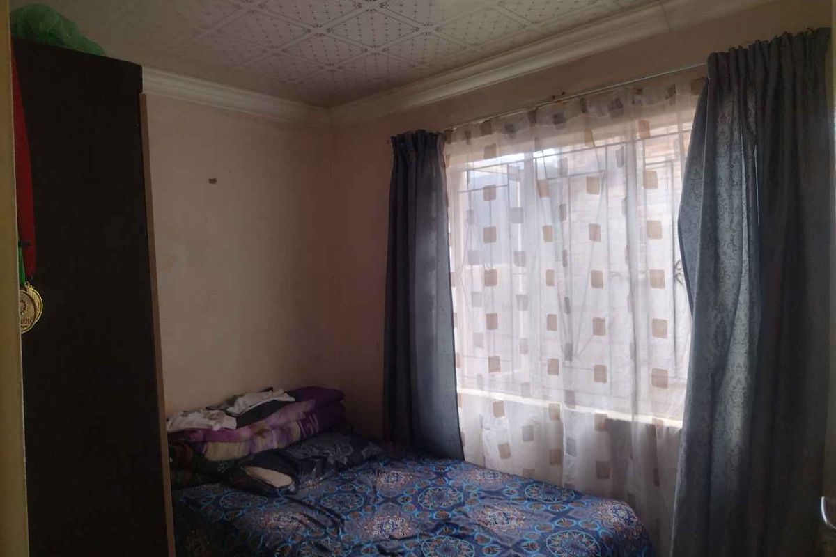A compact bedroom featuring a window with curtains and a textured ceiling finish.
