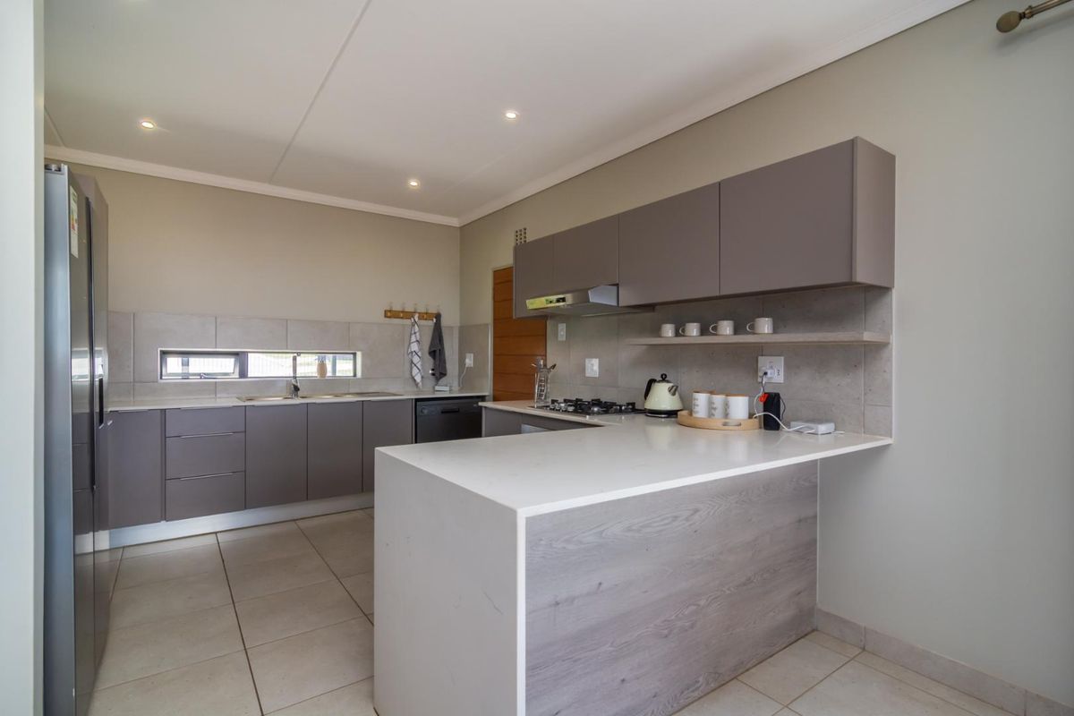 Modern kitchen featuring sleek grey cabinetry, stone countertops, a gas hob with extractor, and tiled flooring in a clean, contemporary layout.